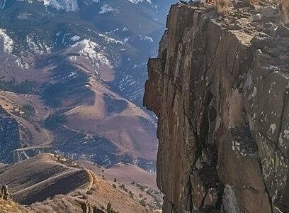 Person flying a drone beside a mountain cliff above a rugged valley