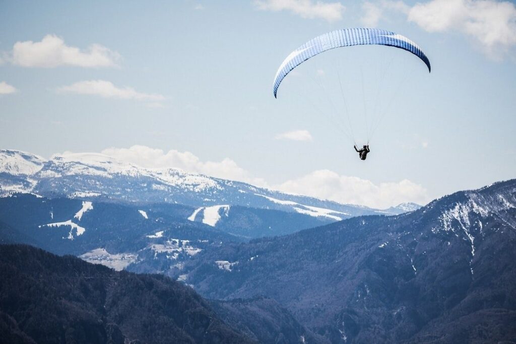 Paraglider gliding above snow-covered mountain slopes under a blue sky