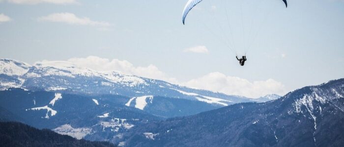 Paraglider gliding above snow-covered mountain slopes under a blue sky