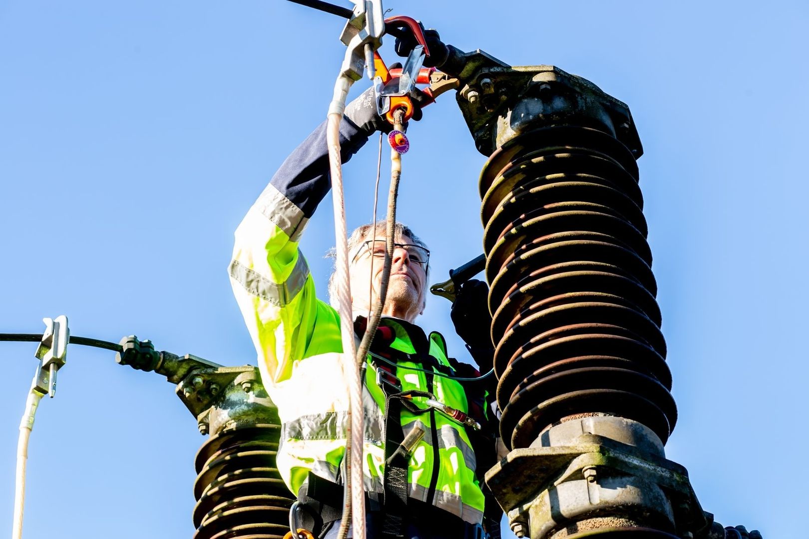 Worker inspecting large ribbed electrical insulators from a safety harness